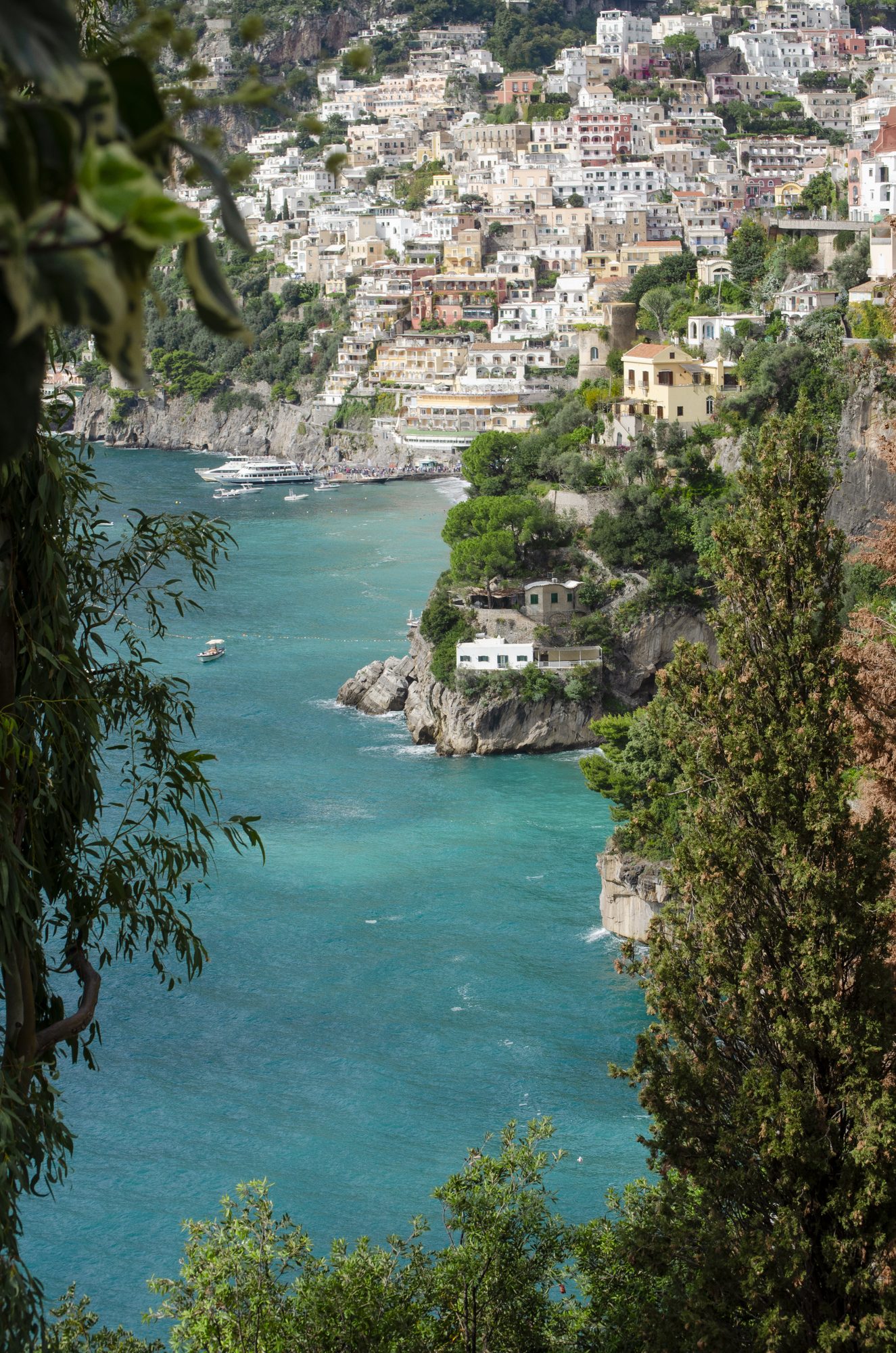Turquoise cove below a cliffside town, framed by trees