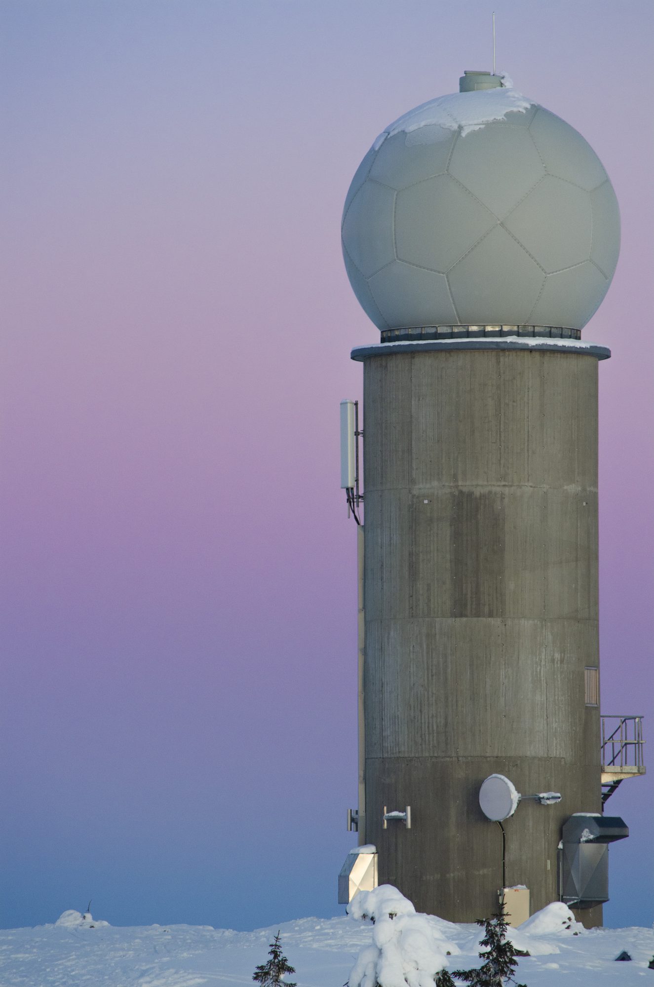 Radar dome tower on a snowy summit against a pink and violet dusk sky