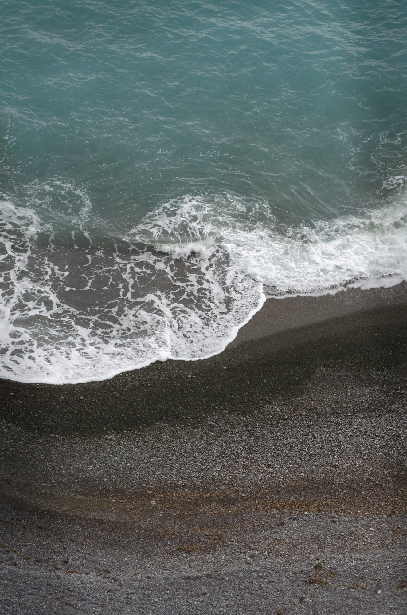 Waves breaking on a dark sand beach, seen from above