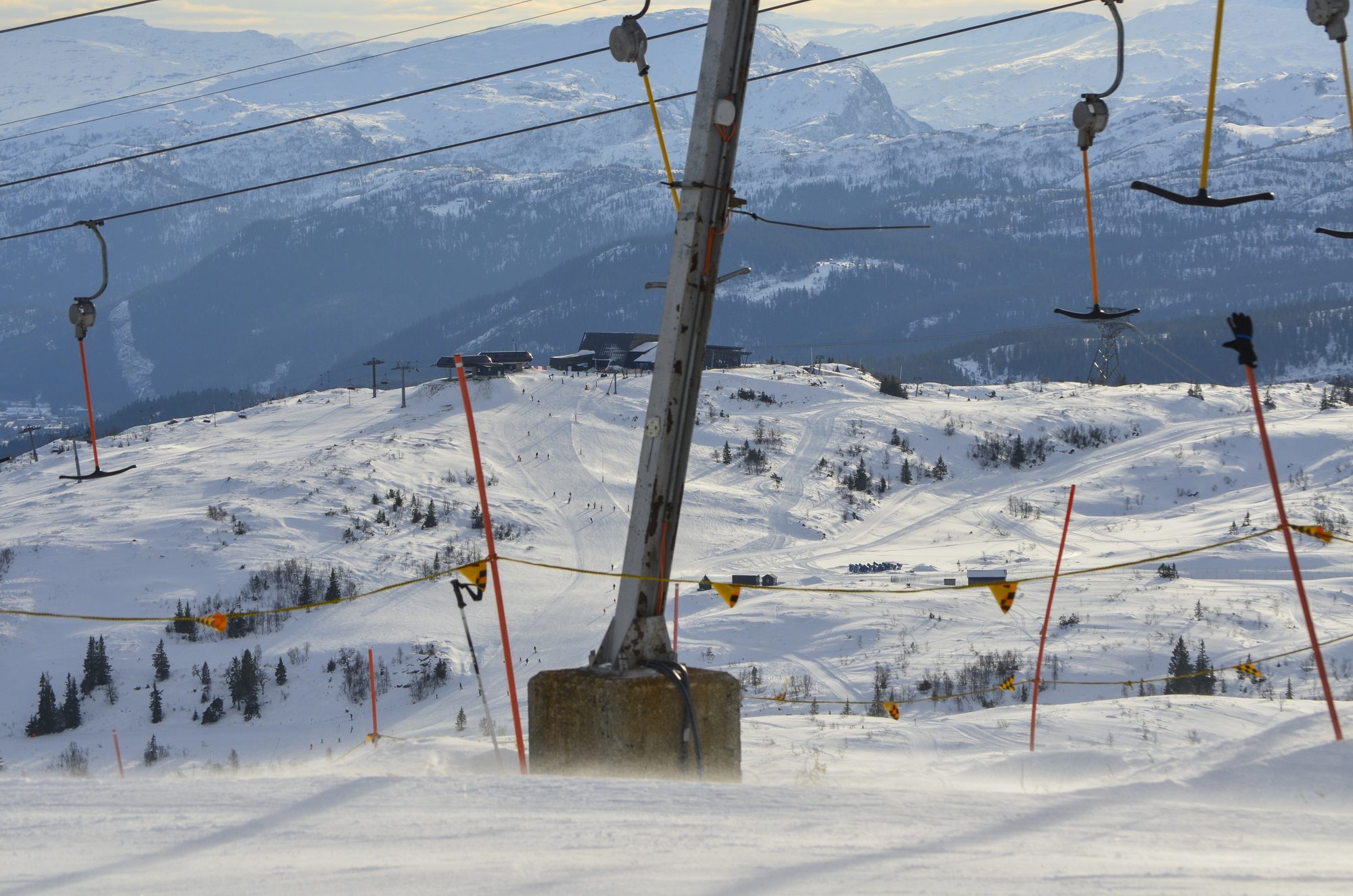 Ski lift pylons over a sunlit snowy plateau with mountains beyond
